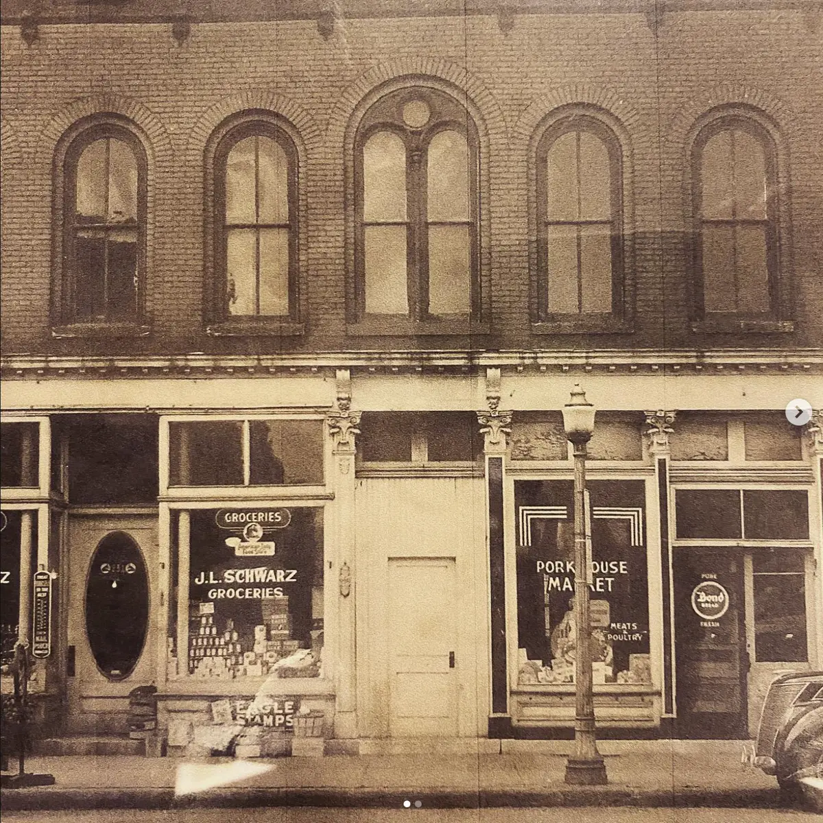 A historic photo of 231 N. Main Street showing the J.L. Schwarz Groceries and Pork House Market storefronts, with arched second-floor windows