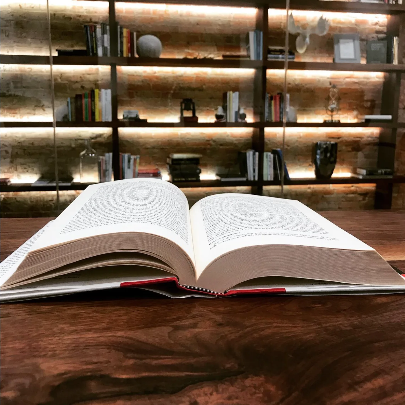 An open book on a live-edge walnut table at The Lodge, with the warm backlit bookshelf wall glowing behind