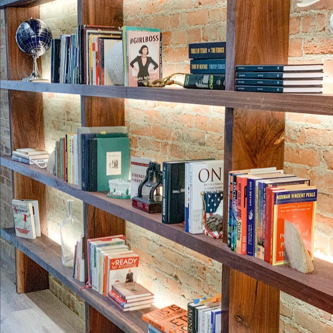 A wall of books on warm-lit wood shelves against restored brick at The Lodge